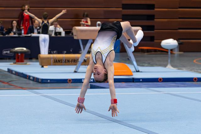 Young gymnast performs handstand on floor mat during routine, demonstrating balance and control at indoor sports event