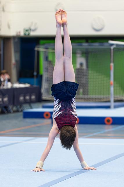 Young athlete performing a handstand on floor mat during indoor training session, demonstrating strength and balance