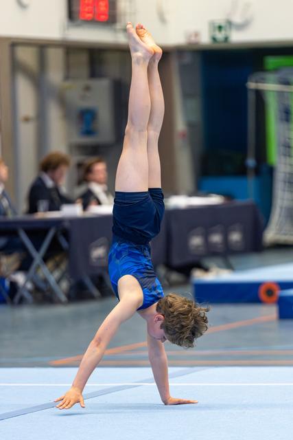 Young athlete performs a vertical handstand on floor mat during routine, displaying strength and balance at indoor sports venue
