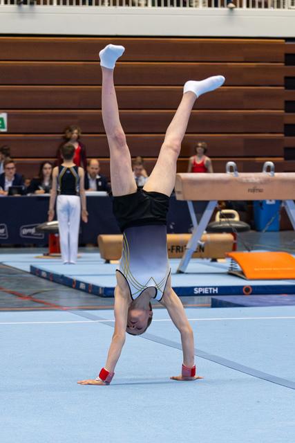 Young athlete performs a handstand on the floor exercise mat during an indoor sports event, demonstrating strength and balance.