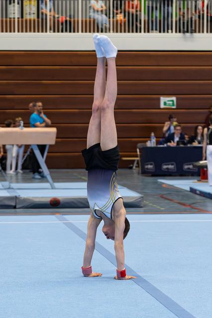 Young athlete performs a handstand on the floor exercise mat during an indoor meet, displaying strength and control