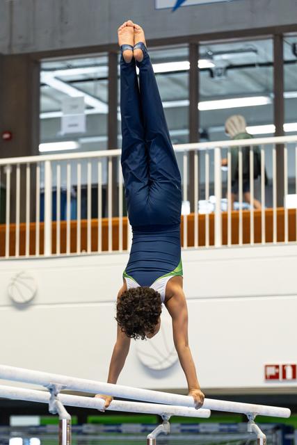 Young athlete performing a handstand on parallel bars, demonstrating strength and balance in an indoor training facility