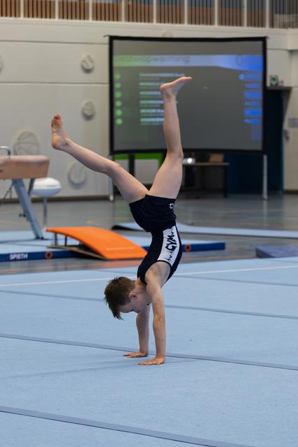 Young gymnast performing a precise handstand on floor mat, legs extended vertically with pointed toes during training session
