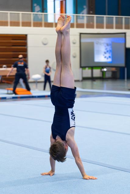 Young athlete performs a handstand on training floor, legs extended upward in perfect vertical alignment