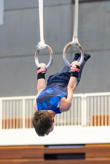 Young athlete performs an inverted hang on the rings during a routine, demonstrating strength and control in the gymnasium