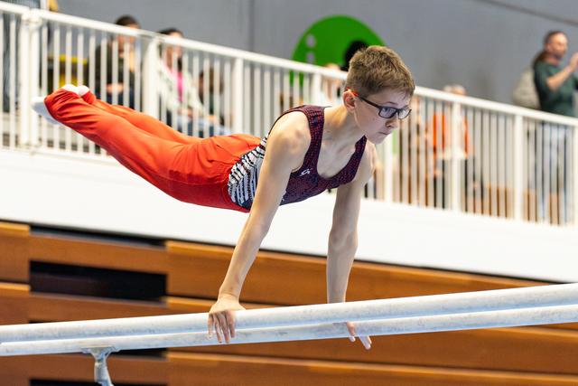 Young athlete performs horizontal balance on parallel bars while spectators watch from gallery above