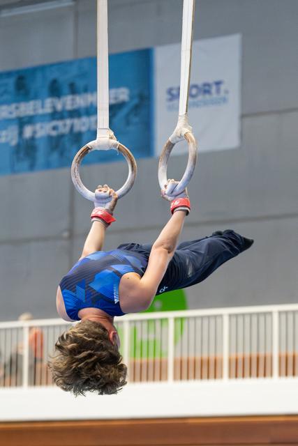 Young athlete performing an inverted position on rings during indoor training session, demonstrating strength and control