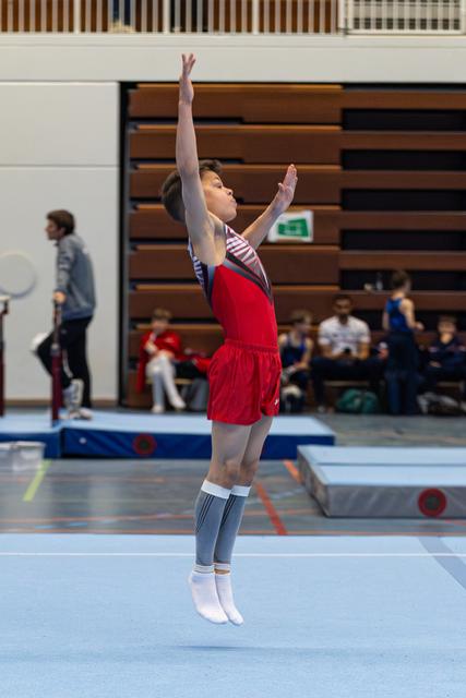 Young athlete jumps with arms raised overhead during floor exercise routine at indoor sports hall