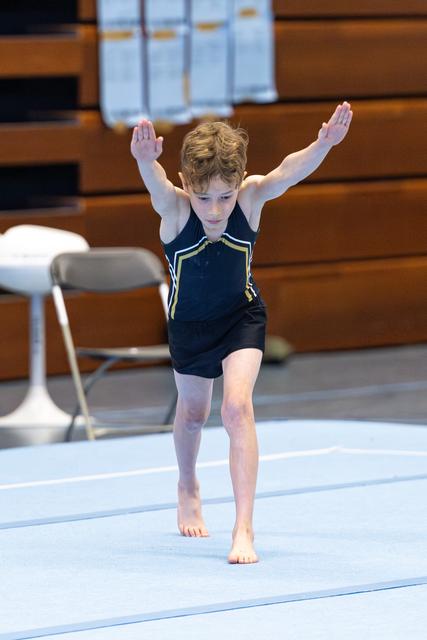 Young athlete lands with arms raised on floor mat, demonstrating focused concentration during routine in gymnasium