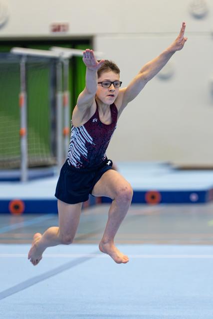Young gymnast in glasses performs a dynamic split leap during floor exercise routine at indoor sports facility