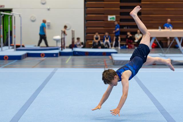 Young athlete performs dynamic handstand mid-routine on floor exercise mat during training session at indoor facility
