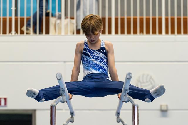 Young athlete performing a straddle hold on parallel bars, looking down with intense concentration during routine