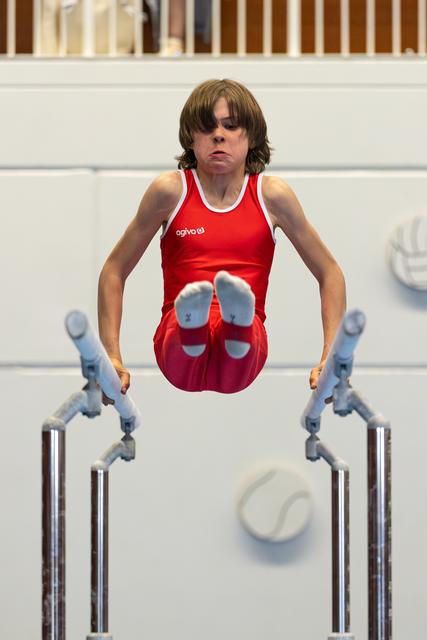 Young athlete performing on parallel bars with focused expression, demonstrating strength and control during routine