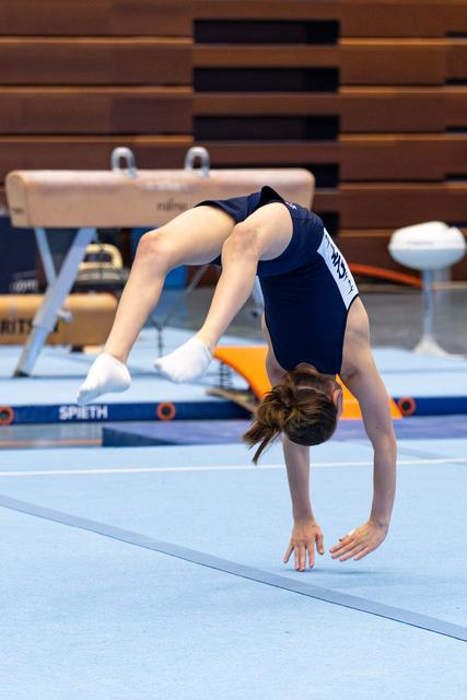 Young athlete performing a backbend with extended legs on the floor mat, demonstrating flexibility during training