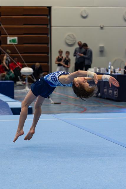 Young gymnast executes a graceful backward aerial layout on floor exercise, demonstrating flexibility and control mid-flight