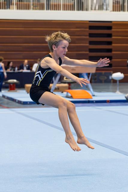 Young gymnast executing a precise landing on floor exercise, arms extended for balance in indoor gymnasium