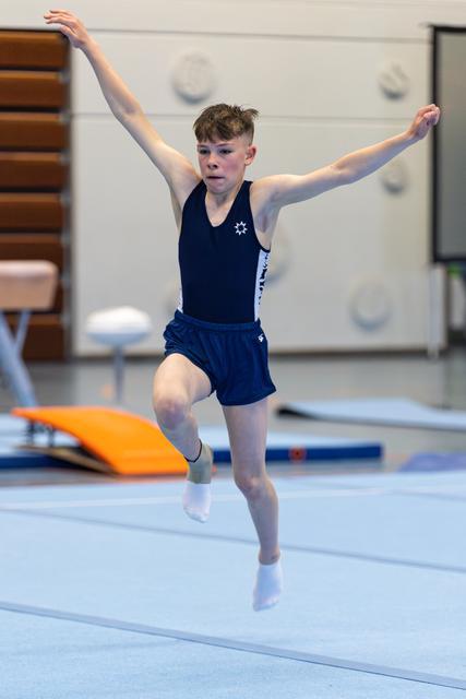 Young athlete mid-leap during floor routine with arms raised, displaying focus and grace in training facility