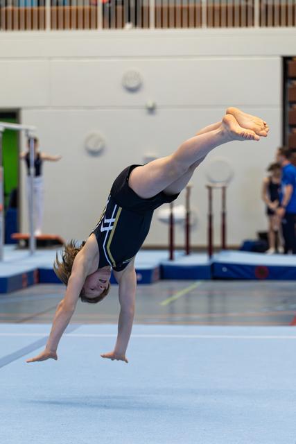 Young gymnast executing a perfect handstand during floor routine, legs extended vertically in a gym setting