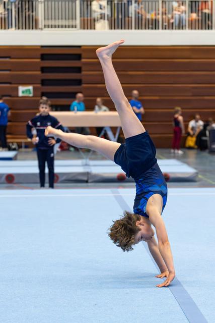 Young athlete executing a handstand during floor routine at indoor gymnastics meet, legs split in perfect vertical line