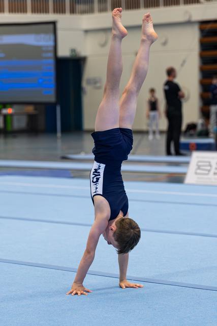 Young athlete performs a vertical handstand on blue floor mat during training, demonstrating balance and strength
