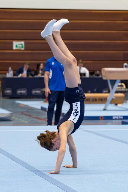 Young gymnast executes a handstand with legs extended upward during floor routine at indoor competition venue
