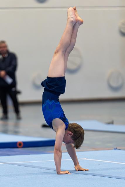 Athlete performs a vertical handstand with pointed toes on blue floor mat during indoor training session