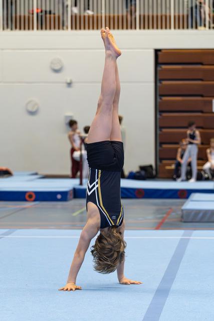 Young athlete executes a perfect handstand on the blue floor mat, legs extended vertically with pointed toes during routine.