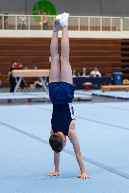 Young athlete executing a handstand on floor exercise mat during training, demonstrating balance and strength in gymnasium