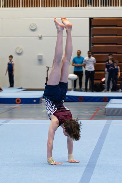 Young gymnast executing a handstand with straight legs on blue floor mat during training session in sports hall
