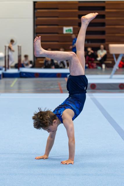 Young gymnast performing a handstand on the floor mat, legs split in the air, during a training session in an indoor facility