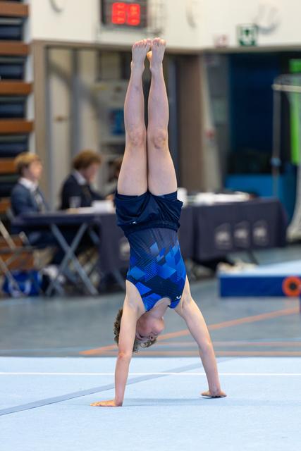 Young athlete performing a handstand on floor exercise mat during training session in gymnasium