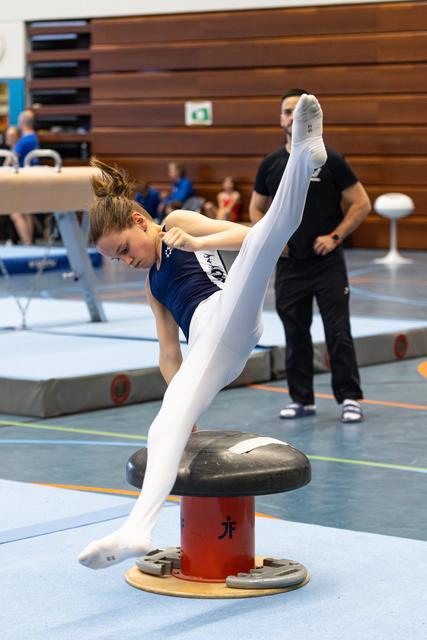 Young gymnast performs split handstand on mushroom apparatus during floor routine at indoor sports competition