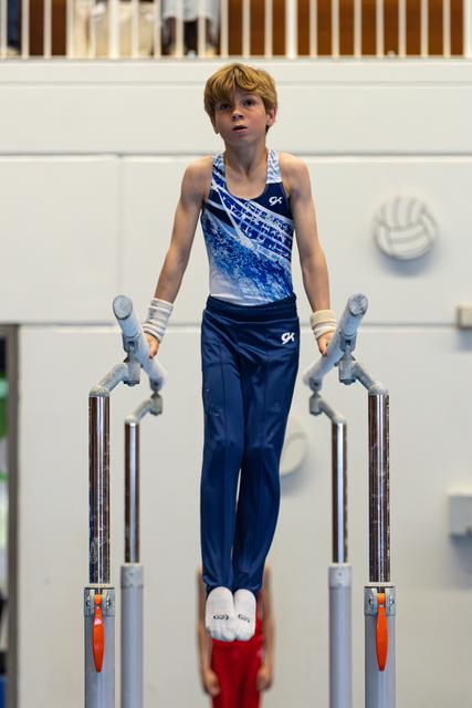 Young athlete in blue gradient leotard performs on parallel bars, focused expression during routine at indoor training facility
