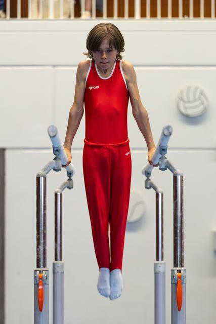 Young athlete in red uniform performing on parallel bars, concentrating during routine with focused expression