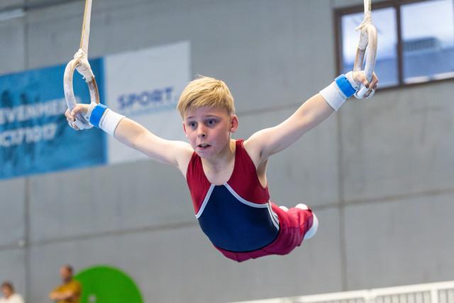 Young gymnast demonstrates strength and focus while performing on still rings at indoor training facility