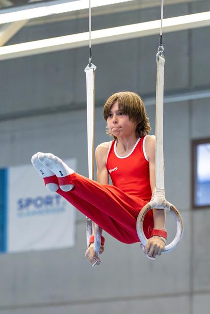 Young athlete in red uniform performing a horizontal hold on still rings, demonstrating strength and concentration