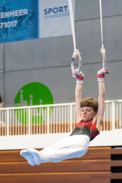 Young gymnast executing a hold position on still rings with straight body and pointed toes during indoor competition