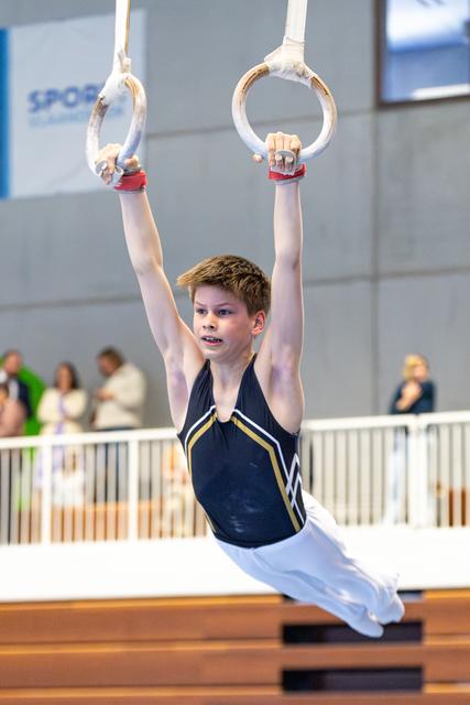 Young athlete demonstrates strength on still rings, arms extended overhead while holding position during competitive routine
