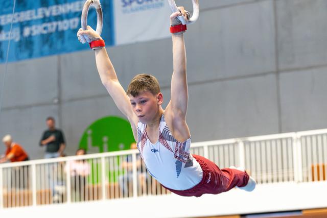 Young athlete performing a still hold position on rings during indoor competition, demonstrating strength and concentration