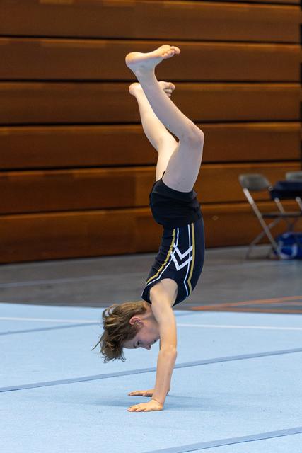Young athlete performs a vertical handstand with pointed toes during floor exercise on light blue mat