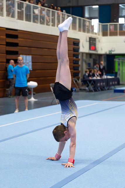 Young athlete executes a precise handstand with straight legs on the blue floor mat during a competitive routine