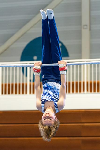 Young athlete in blue leotard performing an inverted hang on the high bar, body extended upward in a vertical line