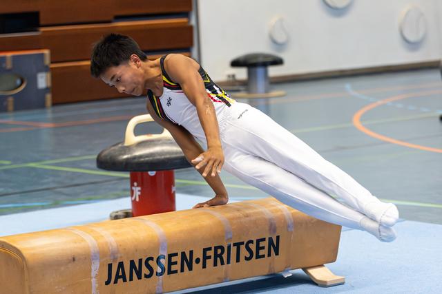 Young gymnast demonstrates intense concentration while performing a support position on pommel horse during indoor training