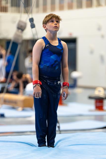 Young athlete in blue outfit with red wristbands stands attentively, gazing upward on competition floor