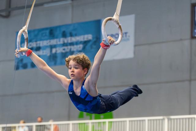 Young athlete performing on rings with focused expression, body horizontal in mid-routine at indoor training facility