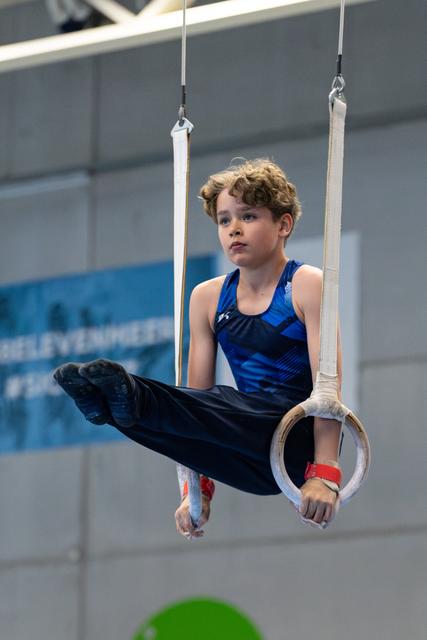Focused young athlete performing an L-sit position on rings during training, demonstrating strength and control in a gymnasium