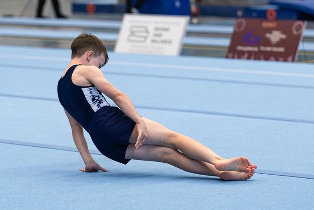 Young athlete performs a seated pike stretch on the blue floor mat during training or warm-up