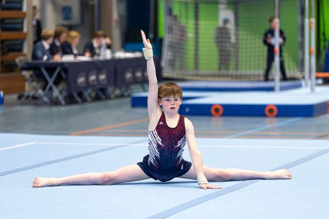 Young athlete performs full splits with one arm raised, displaying flexibility and poise on the competition floor
