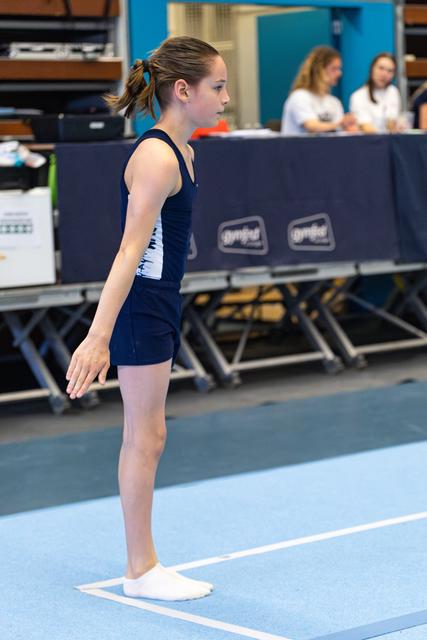 Young athlete in navy leotard stands at attention on the floor exercise mat, focused and ready to begin her routine