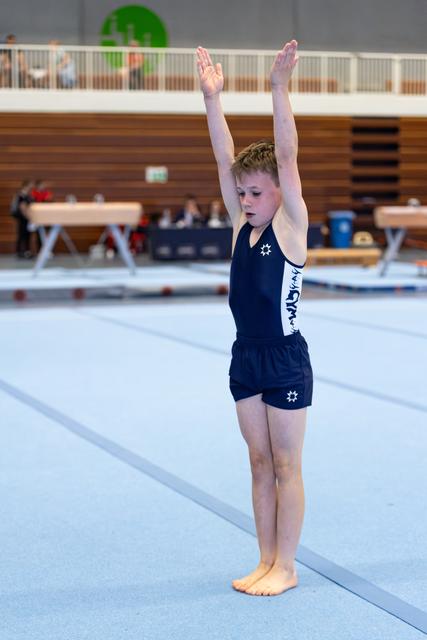 Young athlete in navy uniform stands with arms raised overhead in starting position on training floor